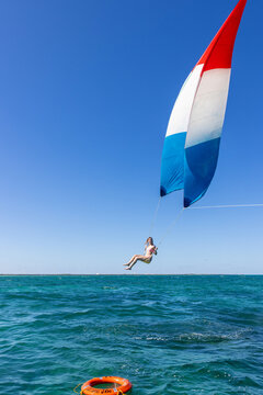 Girl flying over the Caribbean sea during fun activity with a spinnaker parachute ride. The wind is lifting her into the air as she holds on to the kite.