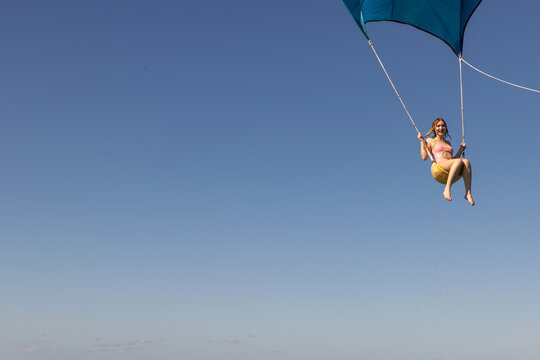 Girl flying over the Caribbean sea during fun activity with a spinnaker parachute ride. The wind is lifting her into the air as she holds on to the kite.