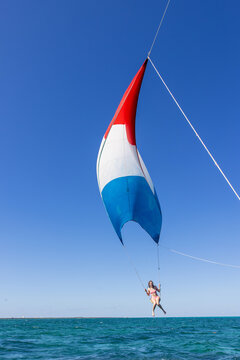 Girl flying over the Caribbean sea during fun activity with a spinnaker parachute ride. The wind is lifting her into the air as she holds on to the kite.
