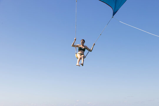 Girl flying over the Caribbean sea during fun activity with a spinnaker parachute ride. The wind is lifting her into the air as she holds on to the kite.