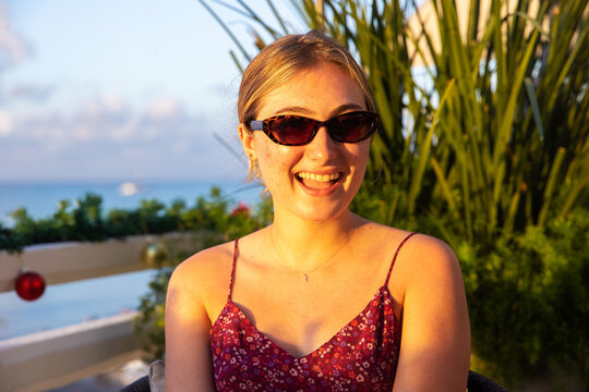 Young woman wearing sunglasses and a strappy dress in the sun. She is smiling and happy while on vacation. 