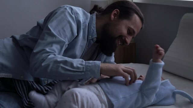 Authentic Bearded Long-haired Young Neo Father And Newborn Baby Looking Each Other Smiling On Bed. Dad Laying With Infant Child. Children, Parenthood, Childhood, Life, Love, Fatherhood, Family Concept