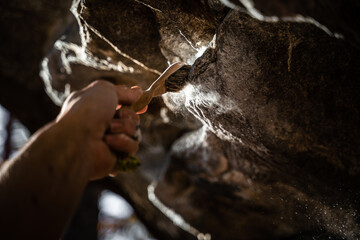 Close up of rock climber's hand brushing a hold with chalk on it on a boulder (climbing outdoors)...