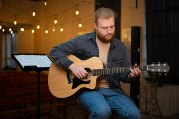 Obraz premium A young guy with a beard plays an acoustic guitar in a room with warm lighting