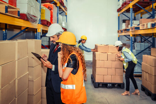 Manager using digital tablet checking order with supervisor and workers checking stock in the warehouse blurred background - Powered by Adobe