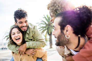 Young adult friends having fun piggybacking outdoors - Group of multiracial people enjoying a day in summer - Friendship concept