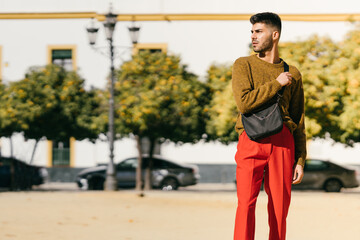 Man in modern style clothing holding a purse while standing on the street