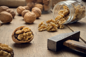 Fototapeta na wymiar Nuts coming out of a glass jar and hammer on a wooden table in a dark environment.. High quality photo