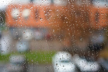 Water droplets on glass with orange buildings and white cars in the background