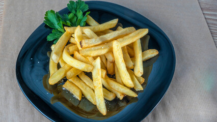 French fries on black dish on parchment background. Tasty golden french fries on a plate.