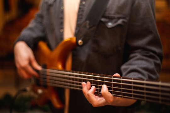 A young guy with a beard plays a bass guitar with five strings