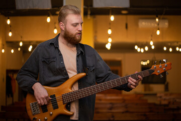 Obraz premium A young guy with a beard plays a bass guitar with five strings