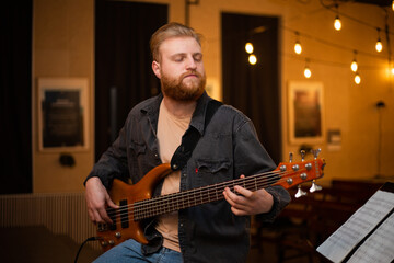 Obraz premium A young guy with a beard plays a bass guitar with five strings