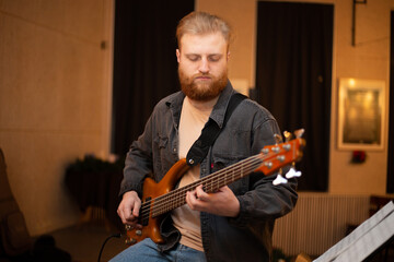 Obraz premium A young guy with a beard plays a bass guitar with five strings