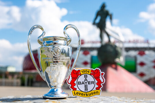 June 14, 2021, Leverkusen, Germany. The emblem of the Bayer 04 Leverkusen football club and the UEFA Champions League Cup against the backdrop of a modern stadium.