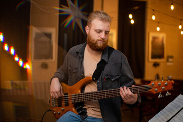 Obraz premium A young guy with a beard plays a bass guitar with five strings