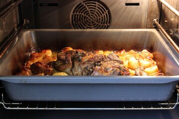Roasting lamb meat and potatoes in a pan in an oven. Shallow depth of field, selective focus