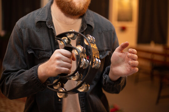 A young guy with a beard plays the tambourine