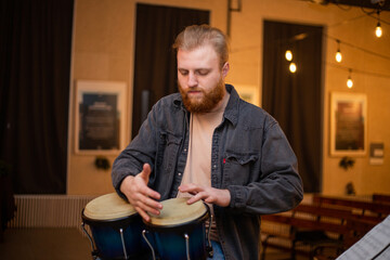A young guy with a beard plays percussion bongos