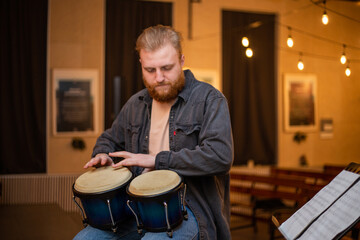 A young guy with a beard plays percussion bongos