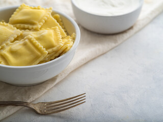 Serving of Italian ravioli, fork and sour cream sauce on a white plate. Pastel shades. There are no people in the photo. Close-up. Restaurant, hotel, cafe, home cooking, culinary blog.