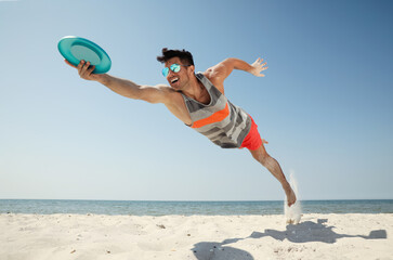 Sportive man jumping and catching flying disk at beach - Powered by Adobe