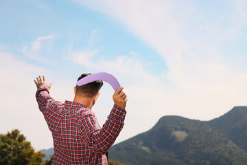 Man throwing boomerang in mountains on sunny day, back view. Space for text - obrazy, fototapety, plakaty