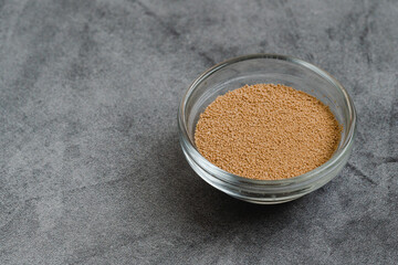 Dry yeast in a glass bowl close up on grey marble background with copy space