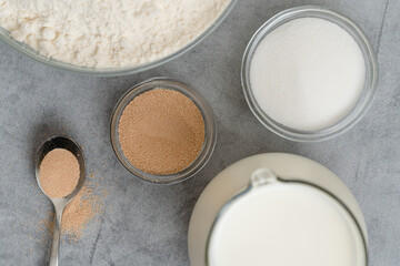 Dry yeast, sugar, flour, and milk on grey marble background, flat lay. Ingredients for baking needs close up
