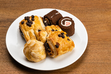 Various baked pastry dessert in white ceramic dish. Assortment of homemade dessert, Eclair filled with corn cream, Danish Pastry filled with chocolate cream and Mini Black Forest Sponge Cake Roll.