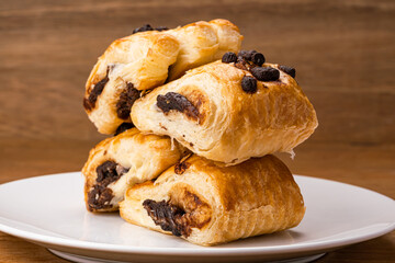 Pile of Danish Pastry filled with chocolate cream topping with chocolate chips in white ceramic dish on wooden table.