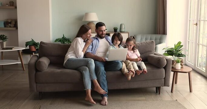 Loving young parents with two kids sister preschooler junior school age brother sit on sofa watch new funny video movie on laptop. Happy family couple with children do shopping buy goods online via pc