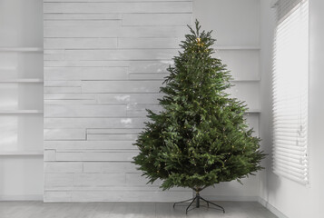 Beautiful Christmas tree with string lights near window in empty room, space for text