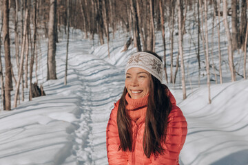 Winter hiking portrait of happy woman smiling in snow forest mountain landscape scenery. Asian woman hiker walking with backpack in cold weather nature landscape