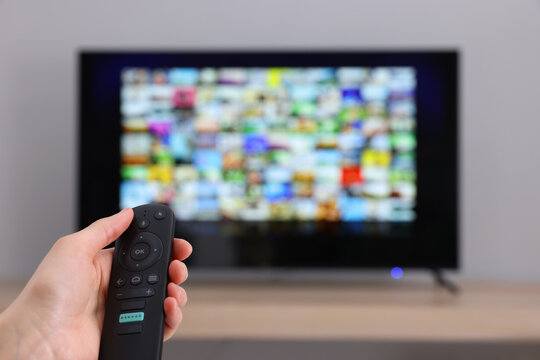 Woman switching channels on TV set with remote control at home, closeup. Space for text