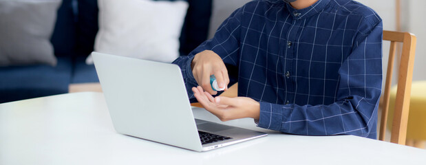 Young asian man work from home with alcohol gel or sanitizer for cleaning hand and protect coronavirus or covid-19, new normal, quarantine and social distancing, businessman using laptop computer.