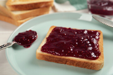 Toast with tasty raspberry jam and spoon on plate, closeup