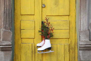 Pair of ice skates with Christmas decor hanging on old yellow door