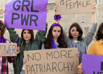 Multi-ethnic female protesters looking at camera holding woman empowerment signs in demonstration for equality.