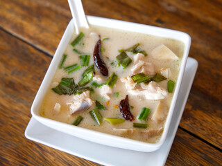 Tom kha kai in ceramic bowl on wooden table. Tom Kha Gai is Thai traditional spicy, sour and hot soup with coconut milk. Thai and Lao cuisines.