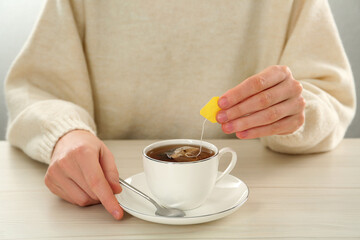 Woman dipping tea bag into cup of water at white wooden table, closeup