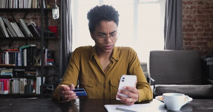 African woman holds debit card and cellphone try to make e-payment through e-bank app, having online ecommerce shopping problem, balance of funds on card not sufficient to pay order, overspend concept
