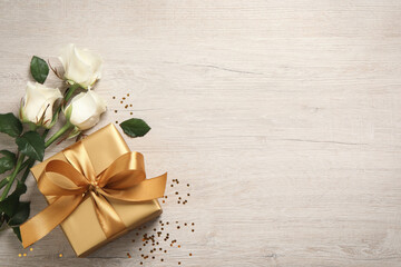 Fototapeta na wymiar Golden gift box and beautiful roses on wooden background, flat lay. Space for text