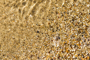 A background of sand, small pebbles and flowing waves on the sea beach. Summer vacation concept