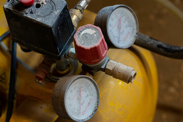 Manometers on yellow industrial air compressor covered with wood dust in a small woodworking shop.