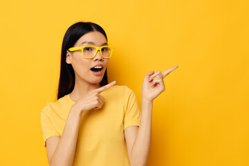 Obraz premium woman with Asian appearance in glasses gesturing with hands copy-space yellow background unaltered