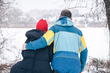 View from the back, a young woman and a man look at the snow-covered lake.