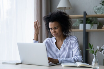 Stressed unhappy young african american woman looking at laptop screen, feeling anxious of made financial mistakes, managing online project, having problems at home office, bankruptcy concept.