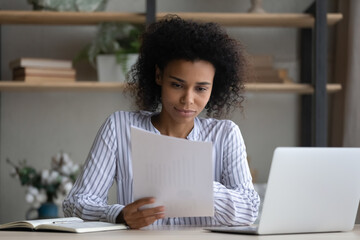 Thoughtful millennial african american multiracial business woman holding paper document in hands,...