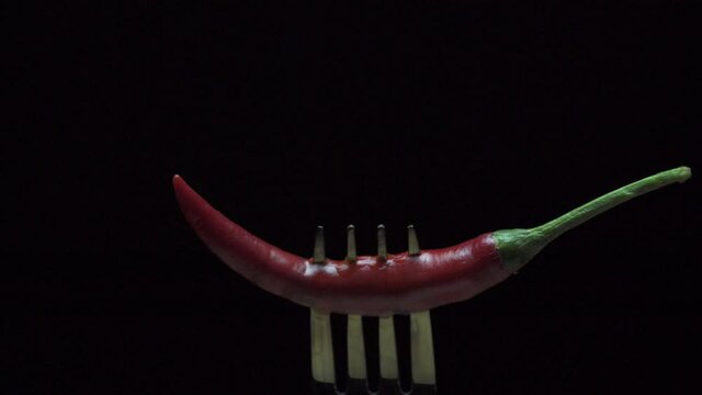 Hot red chili pepper on a fork in flames on a black background. Spicy food concept. Slow motion